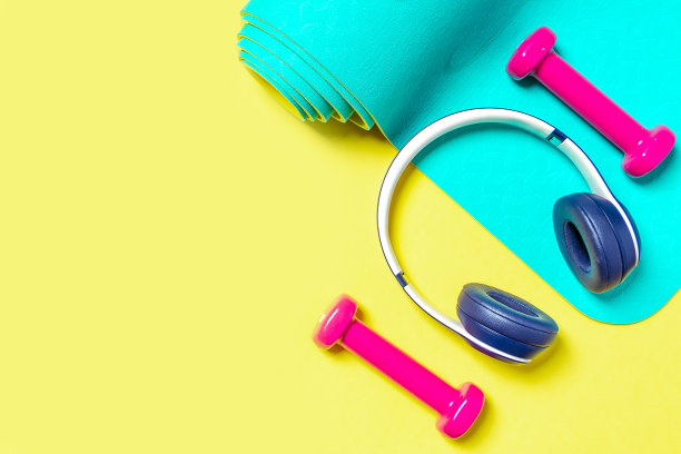 平躺运动和健身设备，粉色哑铃，耳机和薄荷瑜伽垫在黄色的背景。从上往下看，留出文字空间图片下载