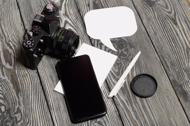 博主的智能手机和照片应用程序。旁边有一本笔记本和一支笔。在演讲中泡沫。以刷过的松木板为背景。图片下载
