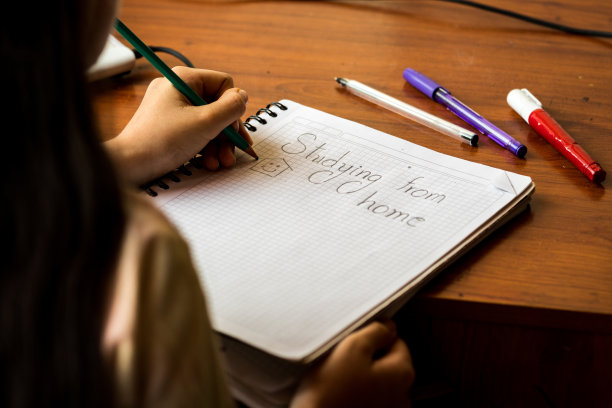 “在家学习”的短语用铅笔写在笔记本上。女孩的手也画了一个带着微笑的房子。一边是笔。图片下载