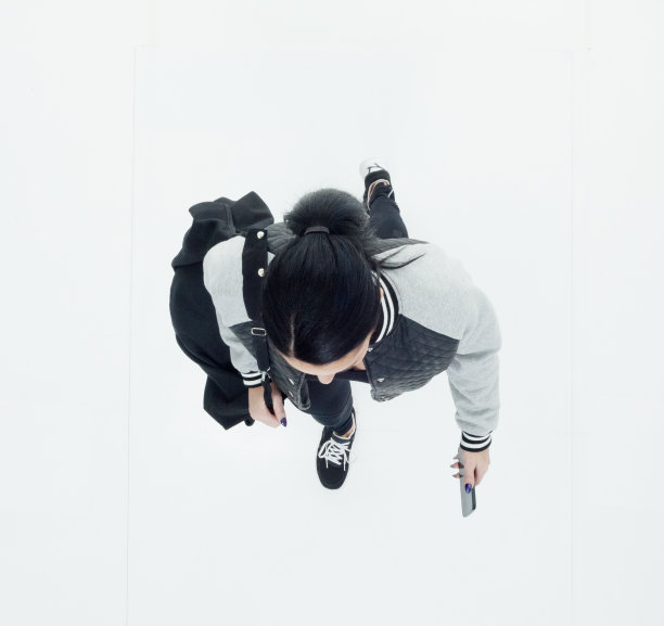 白人年轻女性穿着夹克，拿着包走在白色背景前图片下载