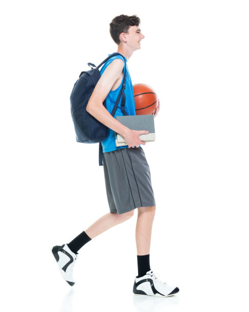 白人年轻男大学生背着背包，拿着课本，用运动球在白人背景前行走图片下载
