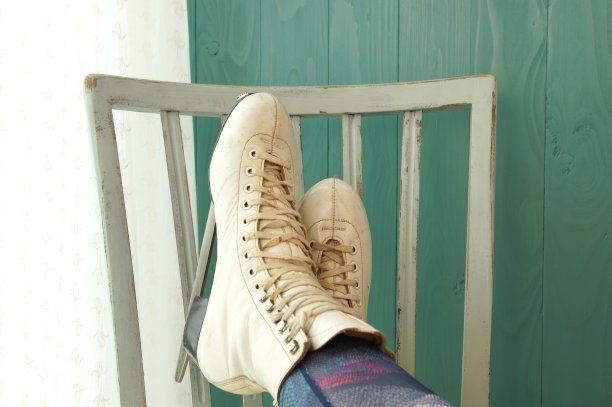 白色女式滑冰鞋上伸着女人的腿坐在椅子上。一双花样滑冰鞋放松和支撑在一个古老的椅子上。图片下载