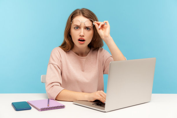 惊讶聪明的女人摘下眼镜，惊讶地张大嘴巴，在笔记本电脑上工作图片下载