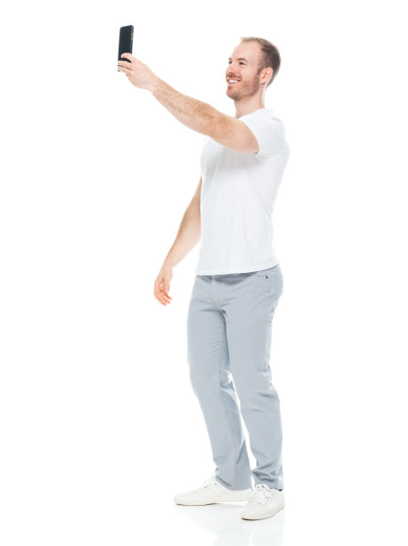 白人男性穿着t恤用智能手机站在白色背景前拍照图片下载