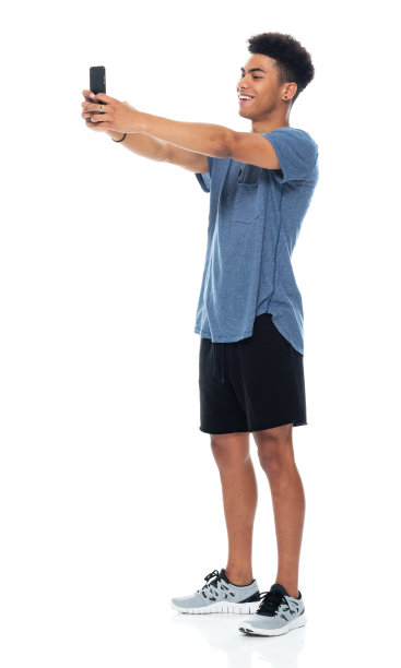 非裔美国青年男性穿着t恤，用智能手机站在白色背景前拍照图片下载