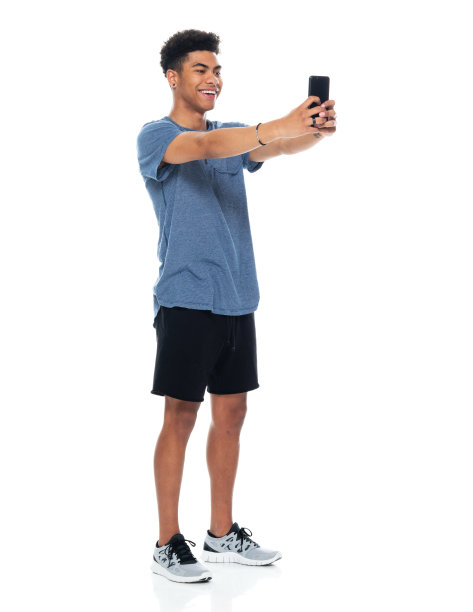非裔美国青年男性穿着t恤，用智能手机站在白色背景前拍照图片下载