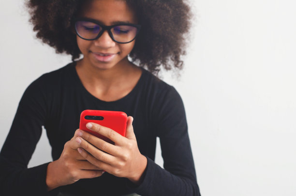 一个皮肤黝黑的女孩手里拿着一部智能手机，看着里面的内容。图片下载