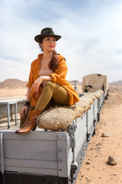 美丽的亚洲女孩穿着牛仔靴和帽子坐在老式木制马车里，眺望着远方图片下载