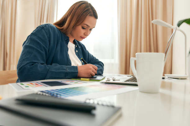 女性设计师在家工作。年轻有创意的女人在休闲衣服上画一些东西，而坐在她的创造性的工作场所在家里图片下载