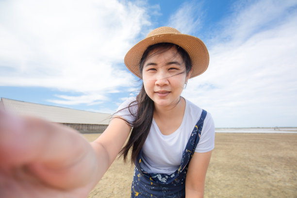 年轻的白人女孩在夏天的帽子在海滩自拍，穿着白色衬衫和草帽的特写。美丽开朗的年轻女子在一个美好的日子里在海滩上玩得很开心图片下载