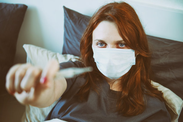 一名染有流感病毒的红发妇女戴着口罩递给医生一支体温计图片下载