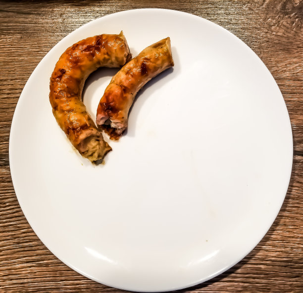 在烤架上烤的天然自制香肠。细长的香肠盘绕在桌面上的盘子上。图片下载