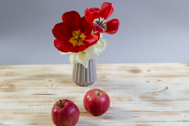 成熟的红苹果和花瓶上盛开的郁金香和水仙花在木制背景上图片下载