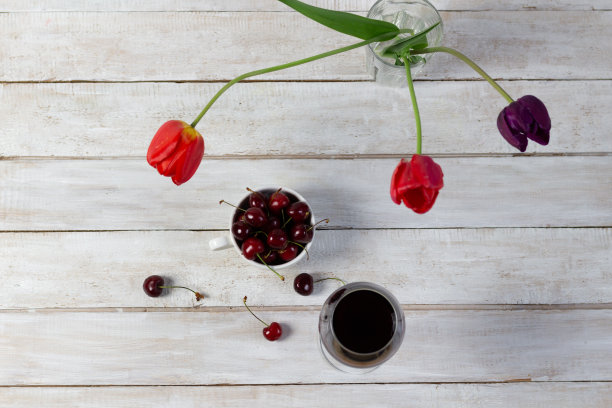 红葡萄酒杯，在白色的木制乡村背景上放着成熟的樱桃和新鲜的郁金香图片下载