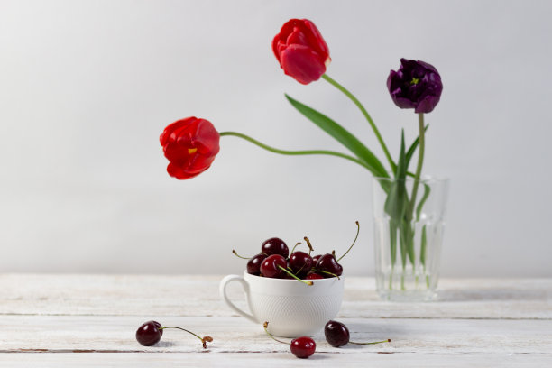 一杯成熟的樱桃在白色木制乡村背景和玻璃与新鲜的郁金香图片下载