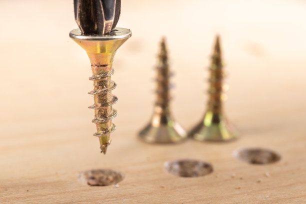 将金属螺钉旋进家具制造用的刨花板中。家庭作坊的小木工工作。光背景。图片下载