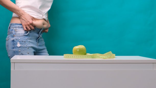 女性肥胖的腹部和青苹果在前景，选择性的焦点。减肥和适当营养的概念图片下载