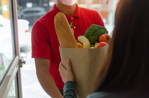 送餐员带着防护口罩穿着红色制服手持新鲜食品套装袋上门上门送餐，以快递、检疫、病毒爆发、外卖为理念图片下载