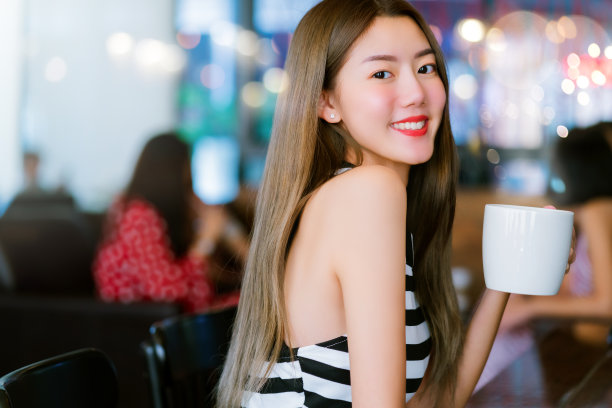 年轻漂亮的亚洲女性在咖啡馆里手拿咖啡杯，笑容灿烂图片下载