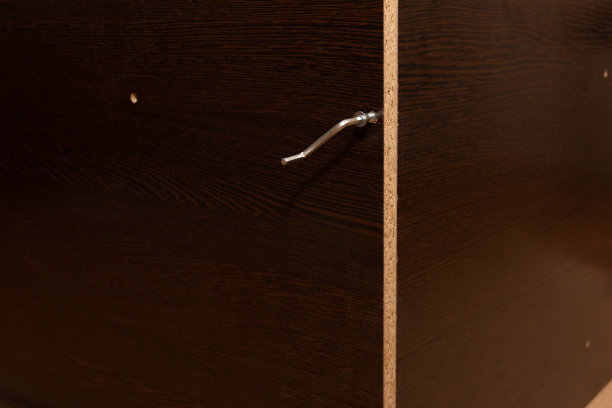 家具内六角键上有一颗螺钉，背景为深棕色的新拼装家具，由层压刨花板制成图片下载
