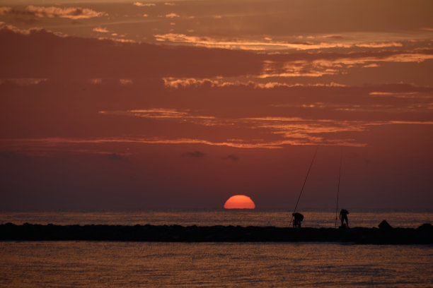 太阳出现在防波堤上的渔民中间图片下载