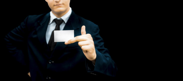 一名身穿蓝色西装的男子在黑色背景下展示名片。图片下载