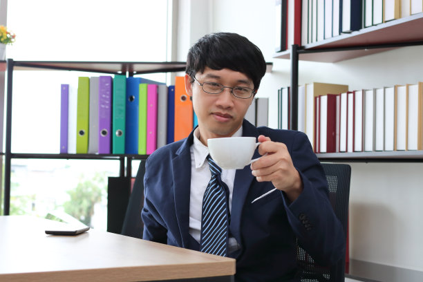 年轻的亚洲商人穿着正装在办公室喝咖啡的肖像。图片下载