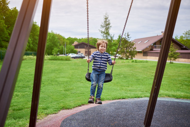 户外肖像可爱的学前班欢笑的男孩荡秋千在操场上图片下载