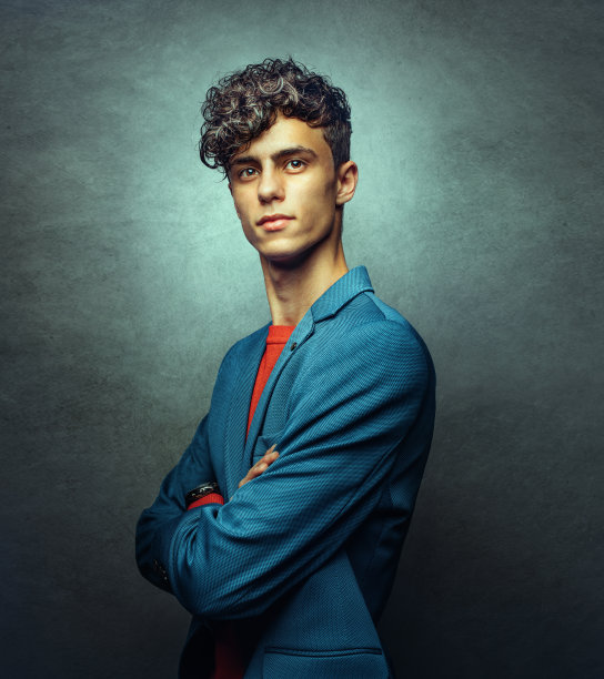 年轻英俊的男人与交叉的胳膊，肖像在蓝色的背景图片下载