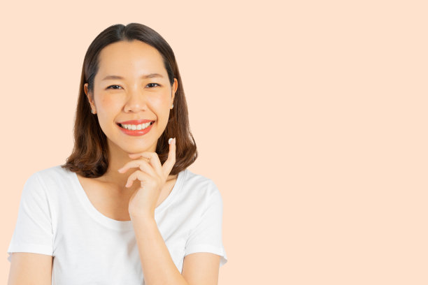 近距离观察年轻美丽的亚洲少女微笑与健康，并使用保湿霜或紫外线防护霜在手指上应用于面部隔离的橙色背景日常美丽生活方式的概念图片下载