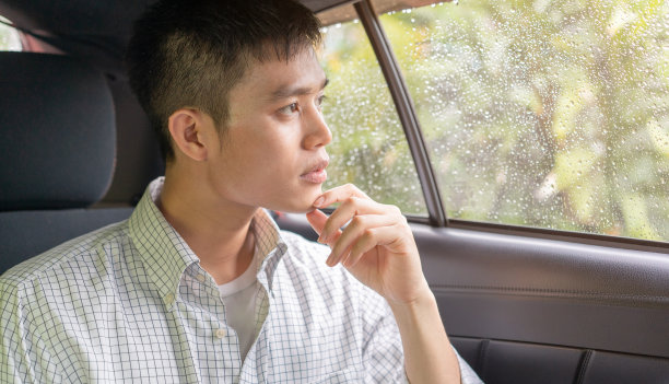 近距离观察年轻的亚洲男子透过车窗，而坐在出租车里思考关系问题与下雨的心情，城市生活方式的交通理念图片下载