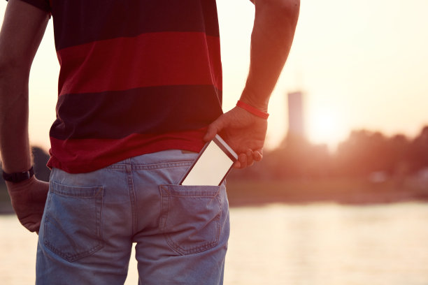 一个男人在河边的口袋里揣着手机。图片下载