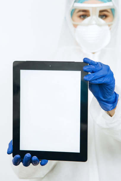 医生穿着防护服、呼吸器、眼镜、手套手持平板电脑/手机。文本。建议医生在新冠肺炎疫情期间呆在家里。新型冠状病毒肺炎图片下载