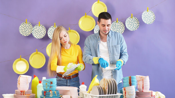 一对辛勤工作的夫妇，妻子和丈夫都站在一张桌子旁边，旁边有一堆脏盘子图片下载