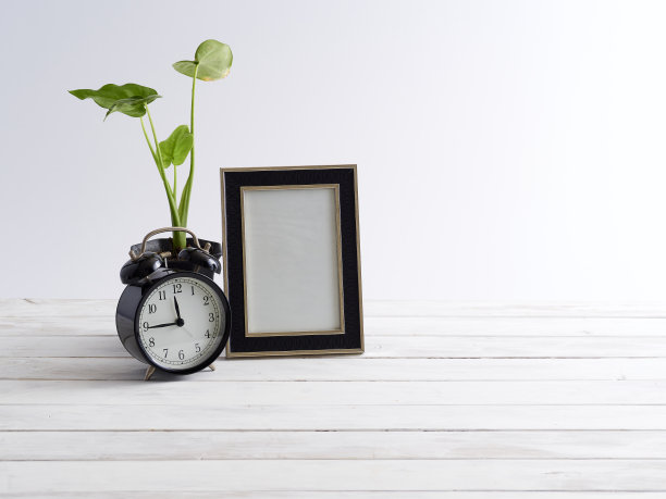 空的相框模拟与黑色闹钟和植物装饰在白色木制架子上。图片下载