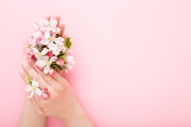 美丽的打扮女人的手与树枝的白色的粉红色苹果花在轻桌子的背景。柔和的颜色。特写镜头。文字或标识的空白位置。自顶向下的观点。图片下载