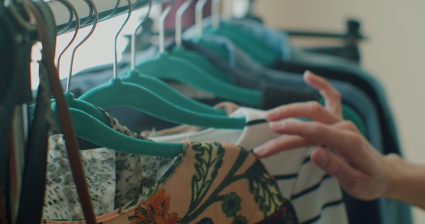 女性手的特写，拿起一个挂着衣服的衣架。一个女人的手在一架子衣服上滑过。女人的手抚摸着一件色彩鲜艳的衣服。特写:挂衣服的衣架。图片下载