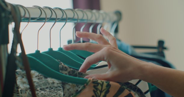 女性手的特写，拿起一个挂着衣服的衣架。一个女人的手在一架子衣服上滑过。女人的手抚摸着一件色彩鲜艳的衣服。特写:挂衣服的衣架。图片下载
