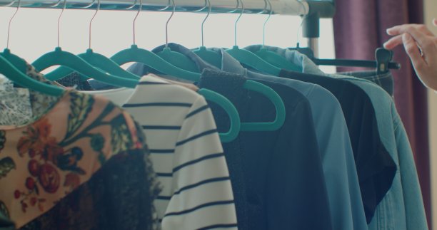 地板上有一个衣架，用来挂衣服。衣架与不同颜色的妇女衣服的背景，全景窗口，特写。图片下载