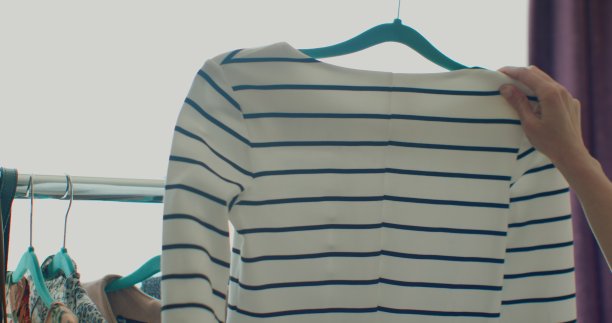 女性手的特写，拿起一个挂着衣服的衣架。一个女人的手在一架子衣服上滑过。女人的手抚摸着一件色彩鲜艳的衣服。特写:挂衣服的衣架。图片下载