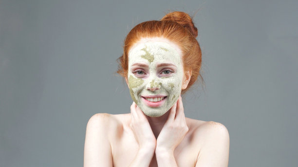 一个迷人的年轻女子的特写肖像与化妆粘土在她的脸上触摸她的脸颊在皮肤护理程序图片下载