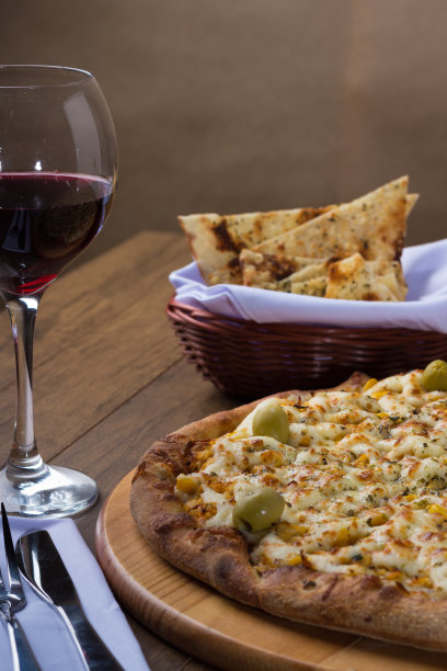 披萨鸡鲶鱼味在木板上。由马苏里拉奶酪，鸡肉，奶油凝乳，绿橄榄，玉米和红番茄酱制成。一杯红酒和面包片。垂直照片2。图片下载