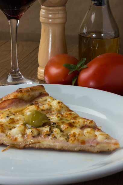 美味的烤沙朗披萨。马苏里拉奶酪，加拿大牛腰肉，奶油凝乳和绿橄榄。切片装在白色的盘子里。采购产品一杯葡萄酒，黑胡椒研磨机，罗勒，橄榄油，刀叉。图片下载