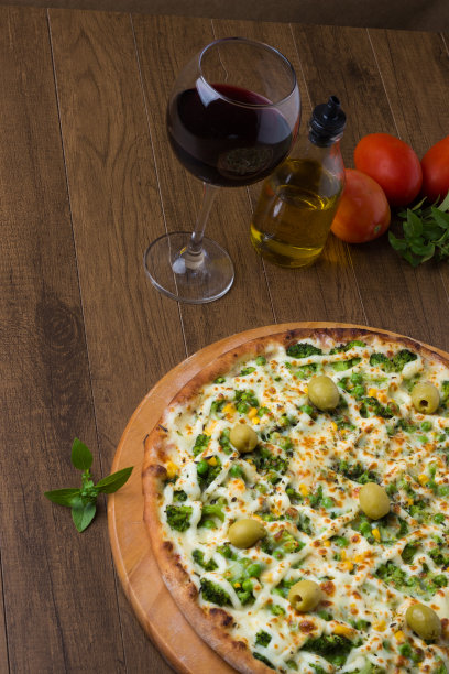 美味的西兰花披萨在木板上。与马苏里拉奶酪、西兰花、玉米、豌豆、橄榄和酱汁一起烘烤。橄榄油，罗勒，红酒和西红柿。垂直的照片。美味的素食菜肴。图片下载
