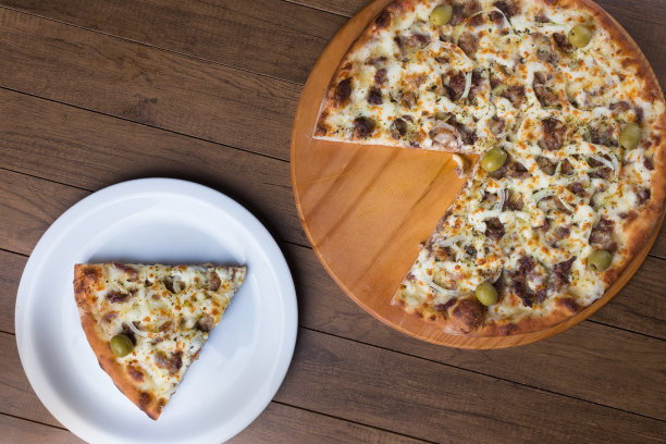 肉披萨放在木板上。由马苏里拉奶酪，picanha肉，洋葱，奶酪，番茄酱和橄榄制成。菲力牛排,肉。一片披萨放在一个白色的盘子和切片的披萨上。照片上的细节。图片下载