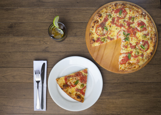 美味的玛格丽特比萨切片由马苏里拉奶酪，西红柿，罗勒叶和绿橄榄。搭配可乐味饮料和柠檬片装饰。前的照片。图片下载