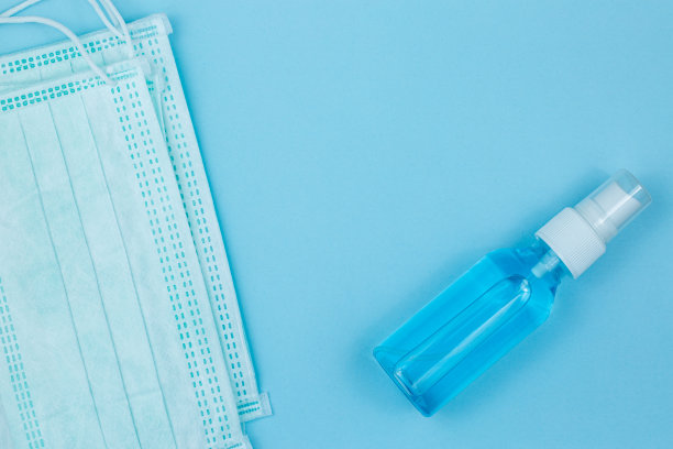 Covid-19冠状病毒的概念。俯视图医疗面罩和酒精凝胶浅蓝色背景与复制空间。面罩和洗手液凝胶泵头瓶。图片下载