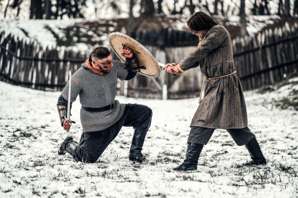 两个身穿盔甲，手持武器的古代战士在雪地里用剑搏斗图片下载