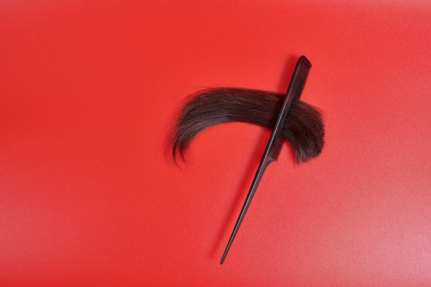 红色背景上的梳子上有一缕剪断的棕色头发。闪亮的头发分叉插在梳子上图片下载