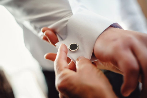 穿衬衫的男人。女人帮丈夫在胳膊上戴上金属的银袖扣。新郎和新娘的手。特写镜头。结婚的那一天。早上好，新郎。图片下载